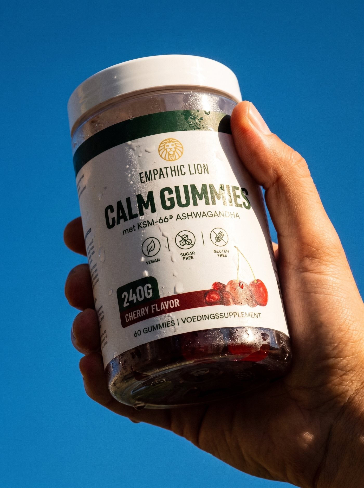 Hand houdt een pot Calm Gummies omhoog tegen een blauwe lucht